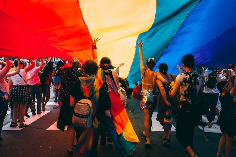 Foto: Menschen marschieren unter einer riesigen Regenbogenflagge