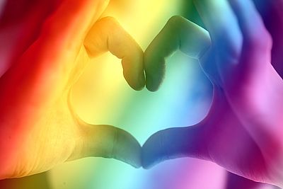 Foto: Herz aus Händen geformt mit Regenbogenhintergrund